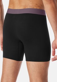 Schwarze Boxershorts mit einem weichen lila Taillenbund. Hergestellt aus glattem Stoff mit enger Passform und flachen Nähten für zusätzlichen Komfort.