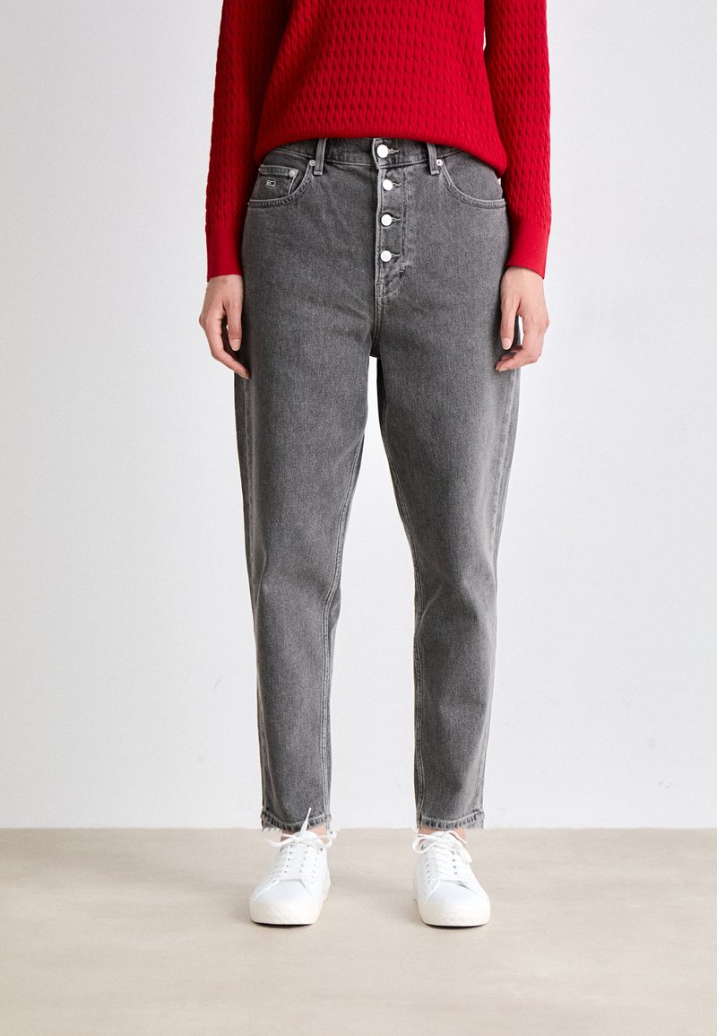 Jeans ajustados de tiro alto grises con un corte recto, cierre de cinco botones y dobladillo deshilachado. Combinados con zapatillas blancas y un suéter rojo texturizado.