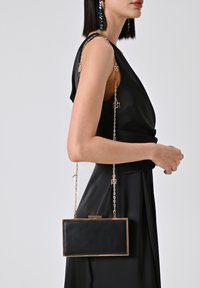 Zwarte rechthoekige clutch bag met gouden accenten en een kettingriem, voorzien van een gladde leren textuur en een sluiting met klapsysteem.