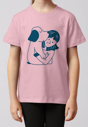 Enfant portant un t-shirt rose avec une illustration bleue d'un chien qui serre dans ses bras et embrasse une personne souriante.