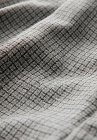 Tissu gris tissé présentant un motif en grille texturé avec de petits carrés, affichant différentes nuances de gris et une finition textile douce.