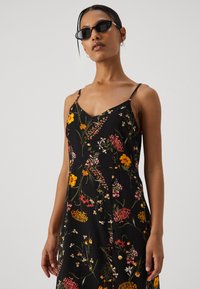 Svart blomstret kjole med tynne stropper, med fargerike blomster og blader i rosa og gule toner. Glatt stoff, avslappet passform, midtlengde.