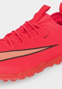 Έντονα κόκκινο αθλητικό παπούτσι Nike με ανάγλυφη σόλα, κλείσιμο με κορδόνια, μεγάλο μαύρο σήμα Swoosh και κείμενο NIKE SKIN στο πλάι.