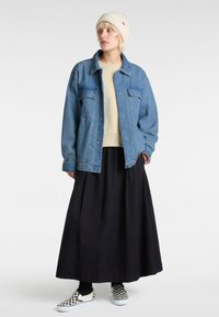 Chaqueta de denim con dos bolsillos frontales, sudadera beige, falda negra y zapatillas de cuadros sin cordones. Un gorro ligero completa el conjunto.