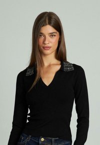 Schwarzer Strickpullover mit V-Ausschnitt und langen Ärmeln, mit strukturierten, verzierten Schultern. Glattes, figurnahes Design.