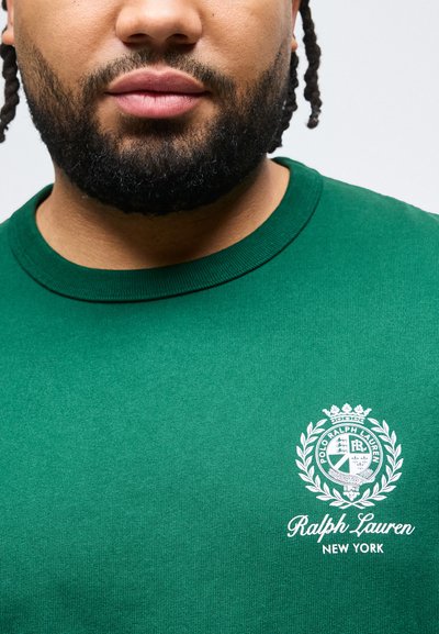 Άνδρας με πλεγμένα μαλλιά και γενειάδα που φοράει πράσινο πουκάμισο Ralph Lauren New York με λευκό λογότυπο και σήμα στο στήθος.
