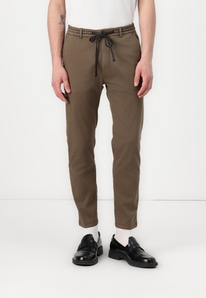Brown, tapered jogger pants with an elastic waistband and adjustable black drawstring. Paired with black loafers and white socks.