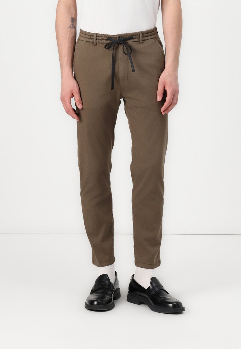 Brune, tapered joggebukser med elastisk midje og justerbar svart snor. Kombinert med svarte loafers og hvite sokker.