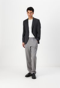 Mörkgrå blazer över en vit t-shirt, i kombination med ljusgrå randiga byxor och svarta skor. Slät tyg, skräddarsydd passform.