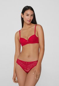 Ensemble de lingerie en dentelle rouge comprenant un soutien-gorge plongeant avec armatures, des bretelles réglables et des slips assortis en dentelle avec un détail de nœud décoratif.
