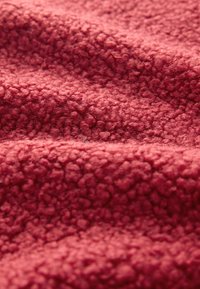 Material textil de culoare roșu închis, cu o suprafață texturată și pufoasă. Materialul prezintă o calitate moale și catifelată, caracterizată prin fibre mici și rotunjite.