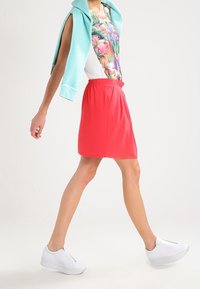 Červená sukně s elastickým pasem, doplněná květinovým topem a světle modrou mikinou přehozenou přes ramena. Bílé tenisky.