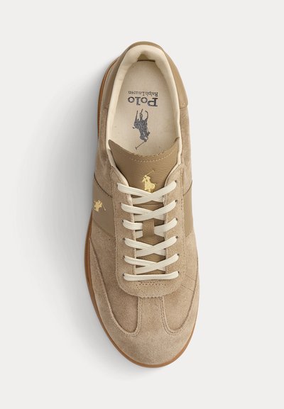 Šviesiai rudos spalvos zomšiniai ir odiniai sportbačiai su baltais raišteliais, auksiniu „Polo Ralph Lauren“ logotipu šone ir liežuvėlyje, ir rudu guminiai padu.