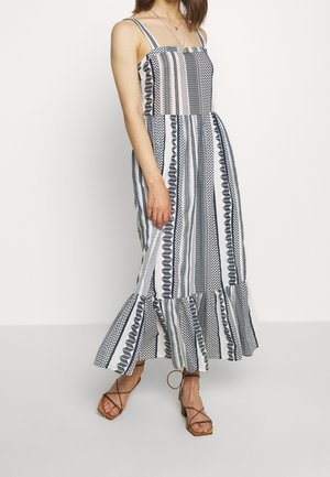 Robe à fines bretelles, à motifs rayés bleu marine et blanc, avec un ourlet à volants. Fabriquée en tissu léger, silhouette fluide.