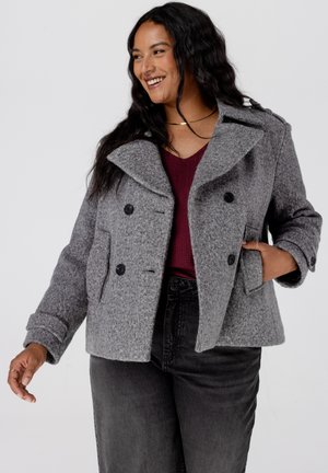 Grijze, gestructureerde zeemanjas met een brede kraag, dubbelgeknoopte sluiting en zijvakken, gecombineerd met een bordeauxrode top en zwarte jeans.