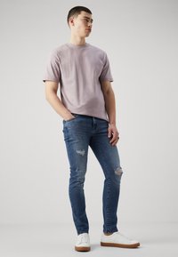 Camiseta de algodón de manga corta en lavanda claro combinada con jeans skinny azul desgastados y zapatillas blancas con suelas marrones.