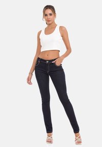 Weißes geripptes Croptop, marineblaue Skinny-Jeans mit kontrastierenden Nähten und weiße Sandalen mit Riemchen. Figurbetonter Stil mit glatter Textur.