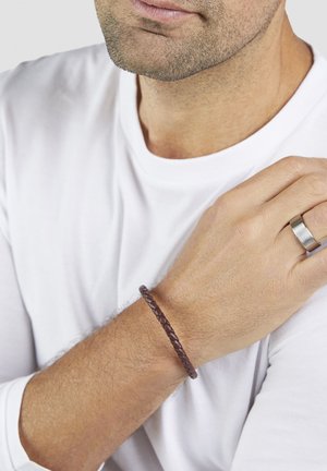 Brown braided leather bracelet worn on the wrist of a person, featuring a smooth texture and a simple, circular design.