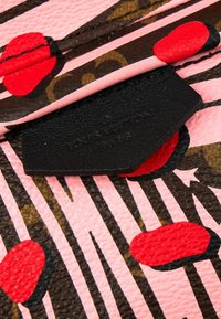 Gros plan d’un tissu texturé avec des rayures et des pois rose, rouge, noir et marron, avec une étiquette en cuir noir partiellement masquée.