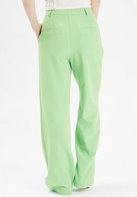 Lichtgroene wijde broek van gladde stof, met twee achterzakken, een op maat gemaakte tailleband en nette stikdetails.
