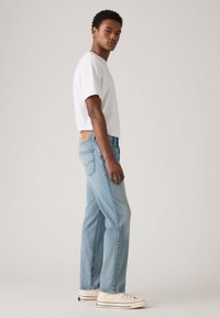 Jeans de ganga azul claro com corte reto, combinados com uma t-shirt branca justa e ténis brancos. Notável aplicação em couro castanho na cintura.