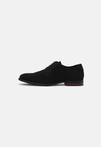 Chaussure pour homme en daim noir avec bout rond, design à lacets et un accent rayé rouge et noir contrastant sur la semelle. Texture lisse.