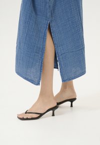 Zila lina kleita ar teksturētu apdari, ar sānu šķēlumu. Melnas augstpapēžu flip-flops ar minimālistisku dizainu.