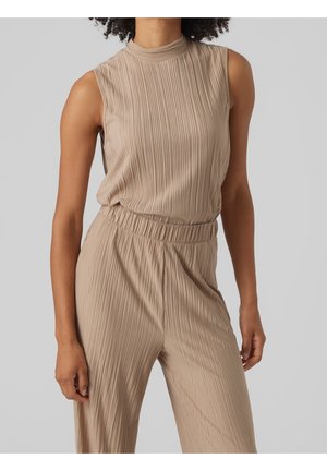 Combinaison beige sans manches en tissu côtelé, avec col montant et taille élastique, portée par une personne sur un fond uni.