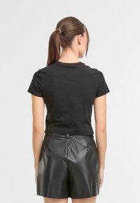 Czarna bawełniana koszulka z krótkimi rękawami, zestawiona z wysokimi, błyszczącymi czarnymi szortami z sztucznej skóry. Gładka tekstura z dopasowanym krojem.