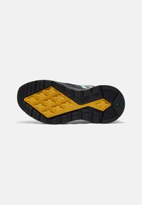 Suola di scarpa sportiva nera e gialla con grip testurizzato e decorato. Presenta una battistrada esagonale e a forma di X per la massima aderenza.
