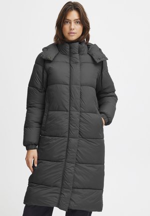 Manteau rembourré noir long avec un col haut, présentant de grandes sections matelassées, des boutons-pression et des poignets élastiques. Texture lisse avec une finition mate.