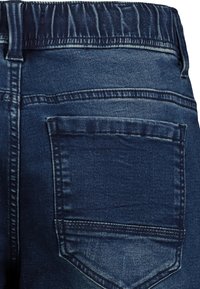 Dark blue denim jeans featuring an elastic waistband, back pocket detailing, and a smooth texture with subtle fading patterns.
