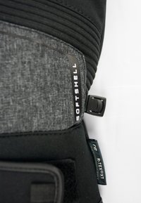 Close-up of black and gray softshell fabric with "SOFTSHELL" and "R-TEXT" labels and an adjustable black plastic buckle.