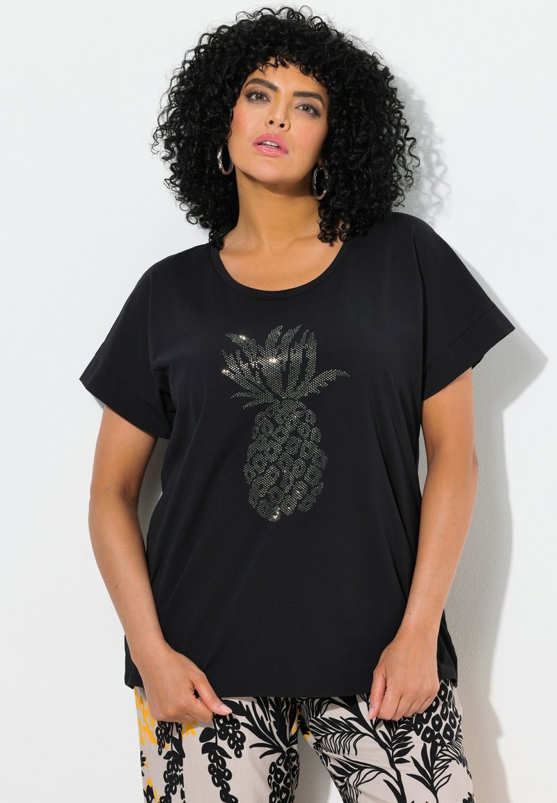Musta lyhytnokkainen t-paita, jossa on hopeinen ananasgrafiikka, joka näyttää teksturoidulta. Yhdistetty kevyisiin, kuvioituihin vaaleisiin housuihin.