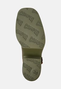 Grön gummisula med upprepad "CAMPER"-logotyp och storlek "38" präglad. Slät yta med rundade klackar och tydlig form.