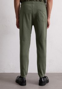 Relaxed-fit groene katoenen broek met zijnaad, een achterzak en omslagzomen, gecombineerd met zwarte schoenen. Gladde textuur.