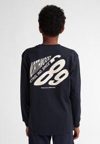 T-shirt a maniche lunghe blu navy con grande testo grafico bianco sul retro, colletto rotondo e vestibilità rilassata. Realizzato in materiale di cotone.