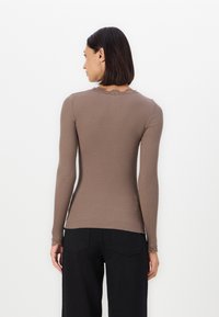 Geribbeld, lange mouwen top in bruin met een gegolfde halslijn en kanten manchetten. Aansluitend ontwerp met textuurstof. Eenvoudige, minimalistische stijl.