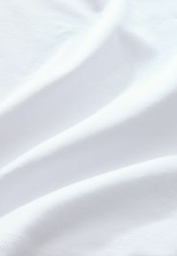 Close-up of smooth white fabric with soft folds and subtle shadows showing texture and light reflection.