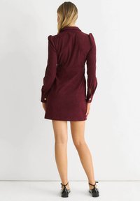 Burgundy corduroy dress with a fitted silhouette, collar, puffed sleeves, button accents on cuffs, and a short hemline.