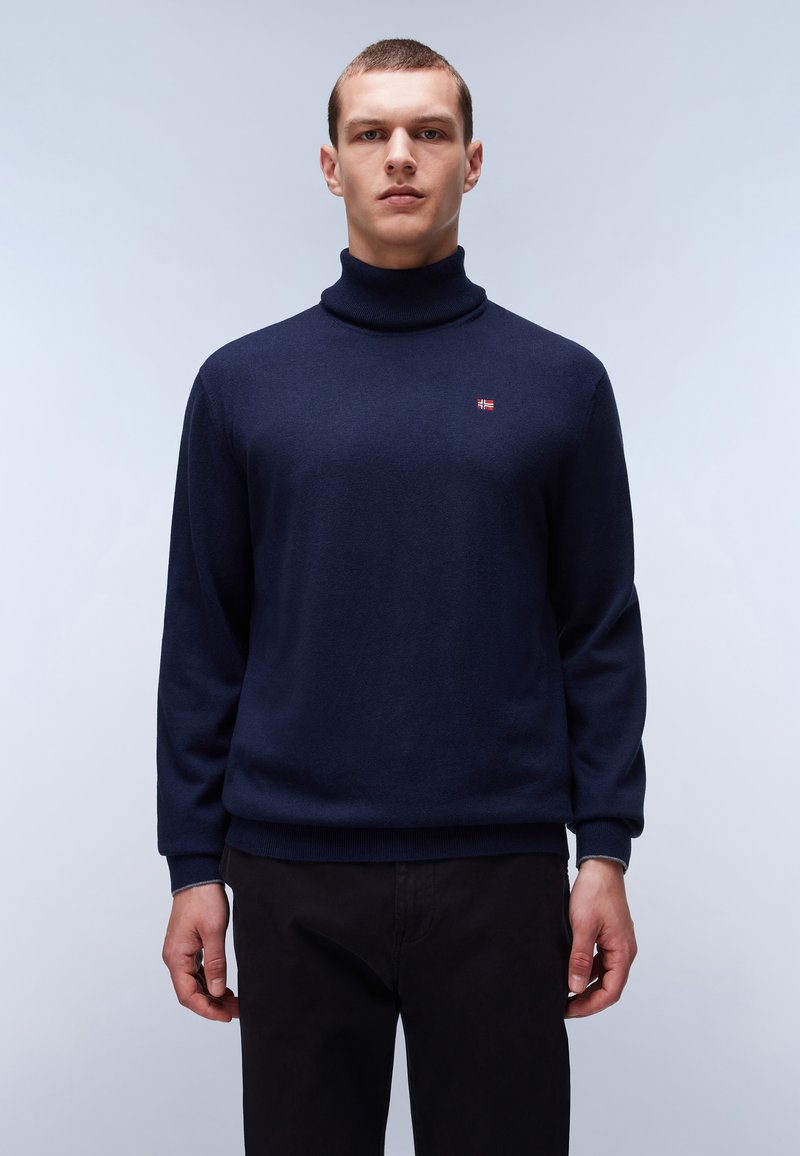 Pullover a collo alto di colore blu navy in un tessuto morbido con polsini a costine, caratterizzato da un piccolo dettaglio con una bandiera rossa e bianca sul petto.
