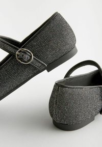Scarpe nere con una tomaia texturizzata caratterizzata da piccoli accenti lucidi. Hanno un tacco basso e una larga cinghia con un dettaglio a fibbia circolare.