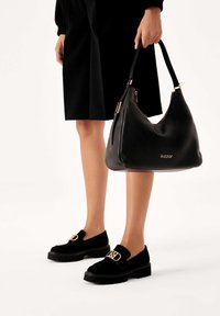 Borsa a tracolla in pelle nera con una texture liscia e accessori dorati, abbinata a scarpe slip-on in suede nero con una fibbia decorativa.