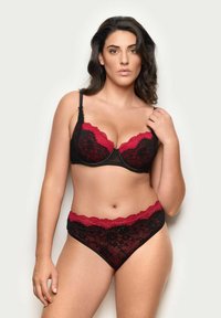 Completo lingerie in pizzo nero con dettagli rossi. Il reggiseno presenta coppe profonde e bordi ondulati; le mutandine a vita alta hanno un design coordinato.