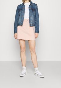 Giacca di jeans, T-shirt bianca e una gonna di jeans rosa con orlo grezzo. Completata con sneakers bianche alte. Outfit semplice e informale.