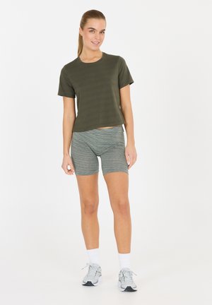 Oliven grøn cropped t-shirt parret med grå stribede cykelshorts. Modellen har hvide sokker og grå atletik sko i en blød tekstur.