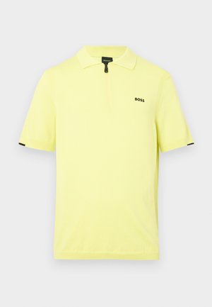 Kortærmet polo-shirt i lys gul bomuld med en lynlåskrave og et lille sort logo på brystet. Sorte detaljer på ærmerne.