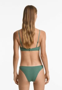 Zelený bikini set obsahující texturovanou, vzorovanou podprsenku s nastavitelnými ramínky a odpovídajícími kalhotkami s nízkým vedením.