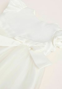White dress featuring a satin bodice, soft tulle skirt, and puffed sleeves. Decorated with a bow at the waist for added detail.