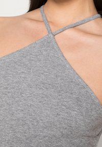 Szary prążkowany top na ramiączkach z dekoltem halter, z cienkimi ramiączkami, ukazujący miękką fakturę i dopasowany krój.